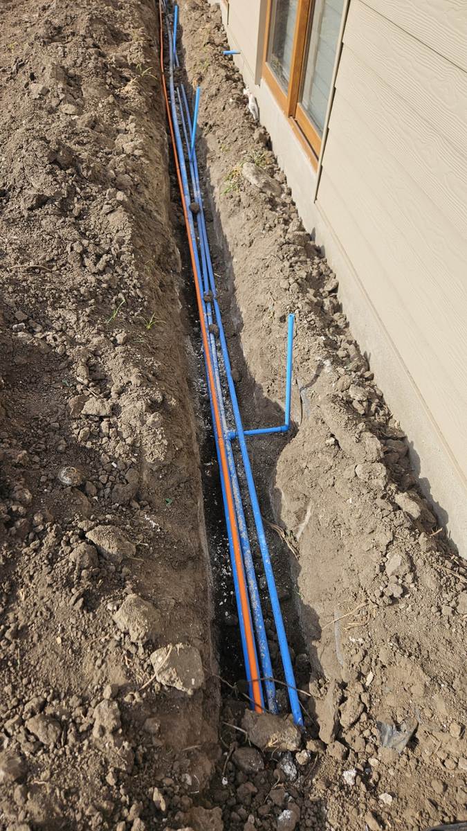 Instalación de tuberías de riego automático en zanja junto a un muro perimetral